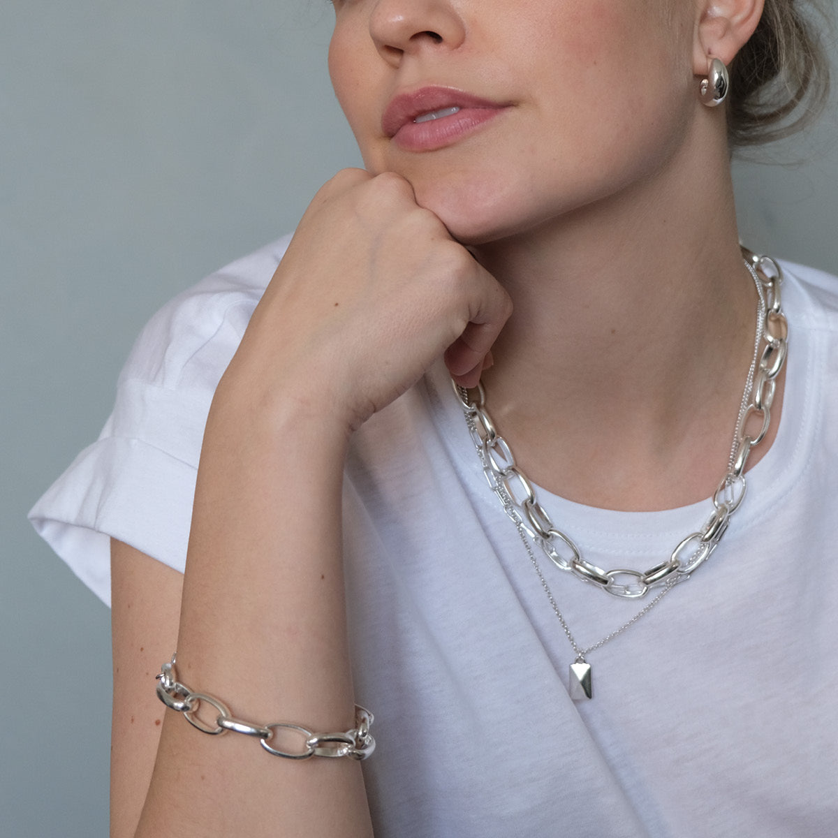 Woman wearing silver chain necklace and bracelet against a neutral background