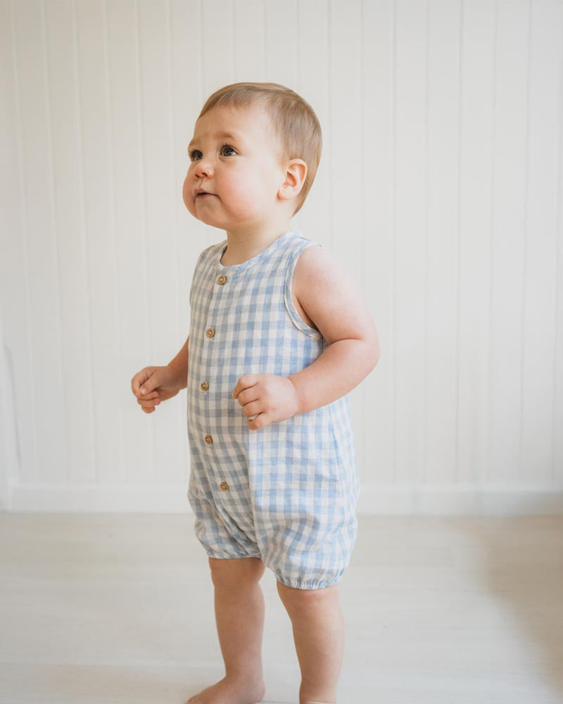 Baby wearing a blue checkered romper against a white background