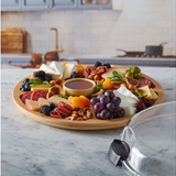 Bamboo charcuterie board with assorted meats, cheeses, fruits, and nuts on a marble countertop.