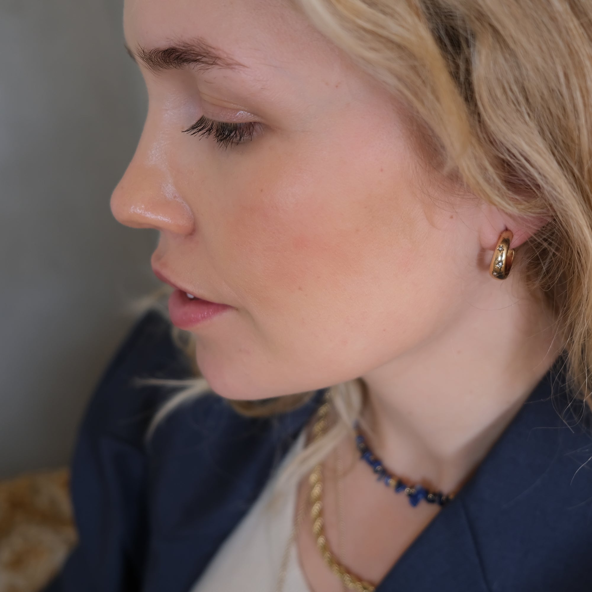 Close-up of a woman wearing gold hoop earrings and a necklace with a blurred background