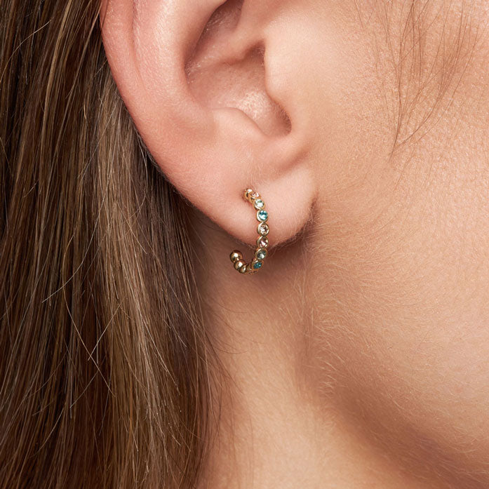 Close-up of an ear wearing a gold earring with turquoise stones.