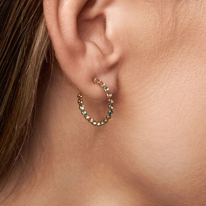 Close-up of an ear wearing a gold hoop earring with gemstones.
