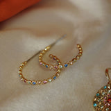 Gold hoop earrings with colorful gemstones on a beige fabric background