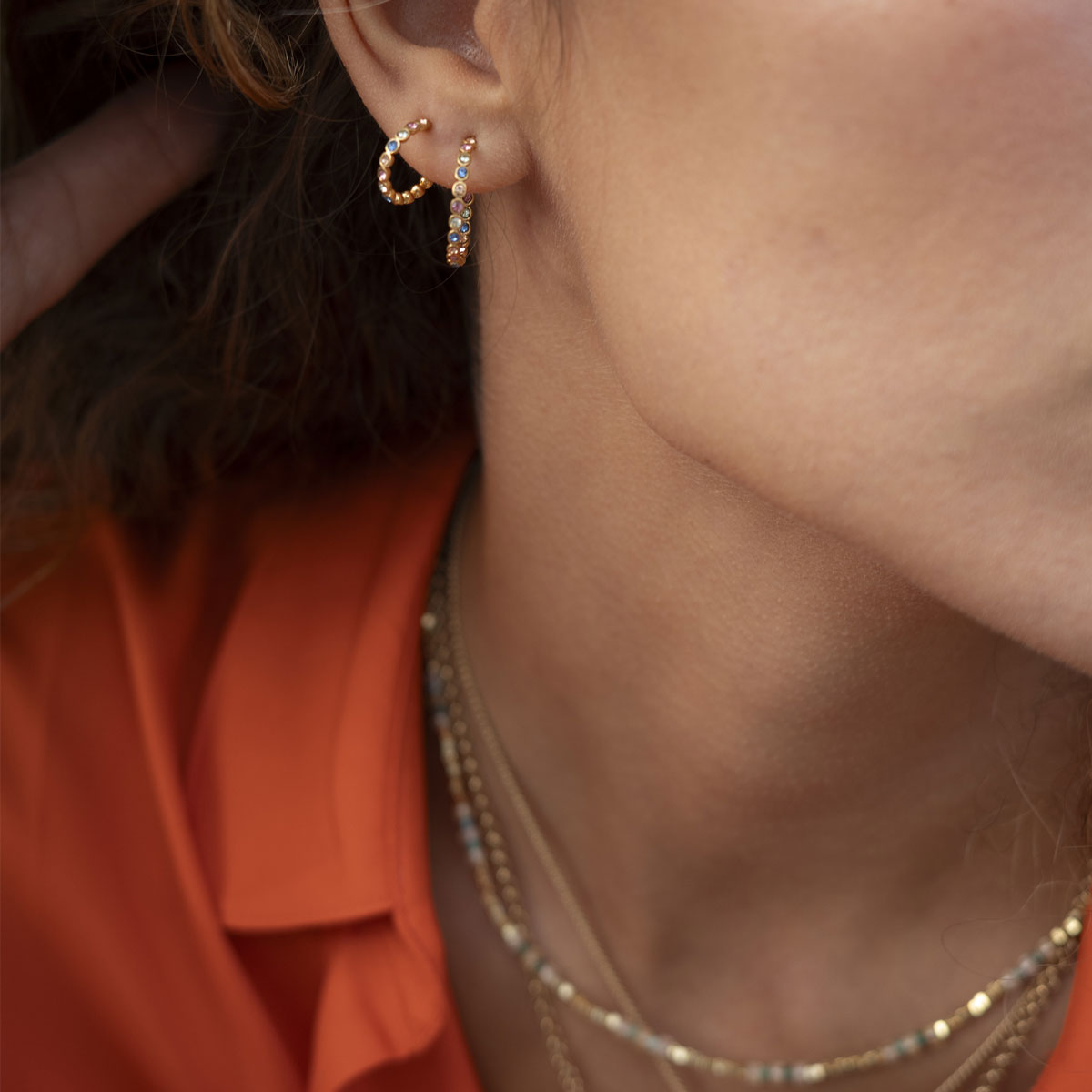 Close-up of an ear wearing gold hoop earrings with a blurred background