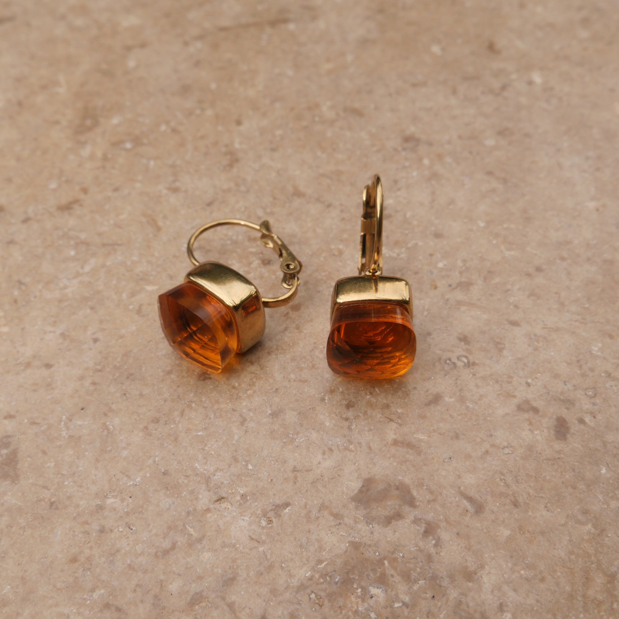 Pair of gold earrings with topaz-colored stones on a beige surface