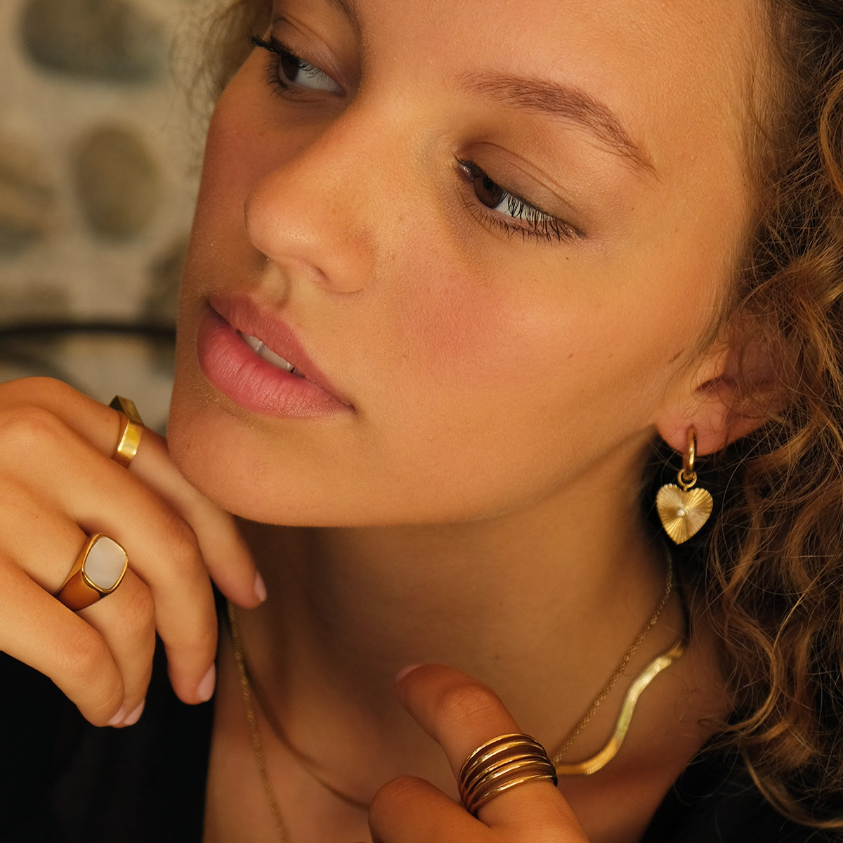 Close-up of a woman wearing gold jewelry including earrings, rings, and a necklace.