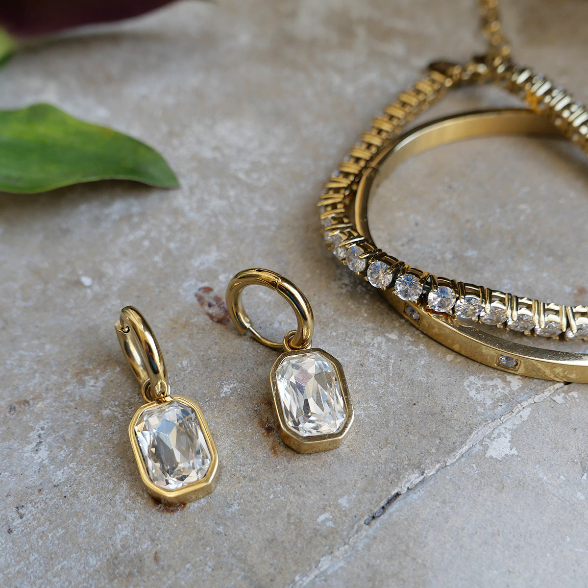 Gold earrings with clear crystals and crystal bracelet on a stone surface