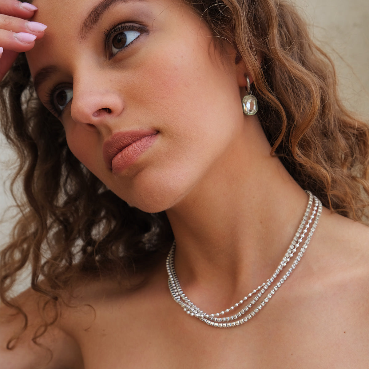 Close-up of a woman wearing a silver necklace and  large crystalearrings against a neutral background