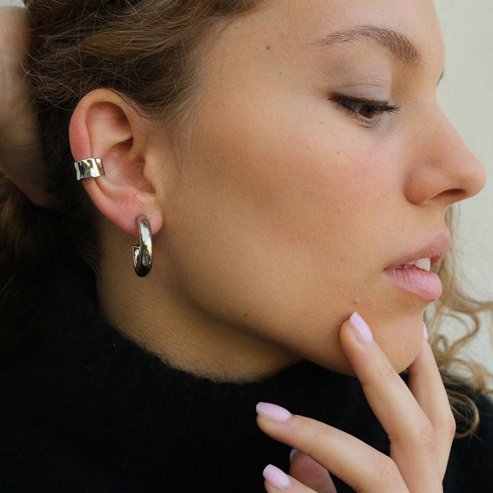 Close-up of a person wearing hoop earrings with a neutral background