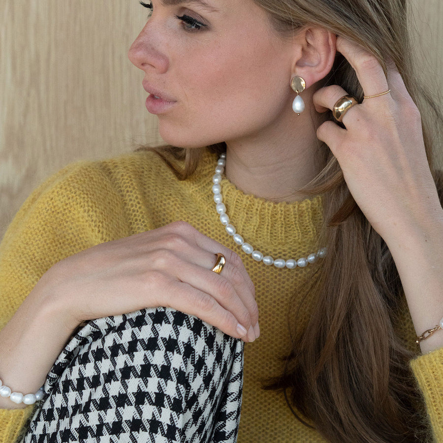 Woman wearing a yellow sweater, pearl necklace, and gold jewelry against a neutral background