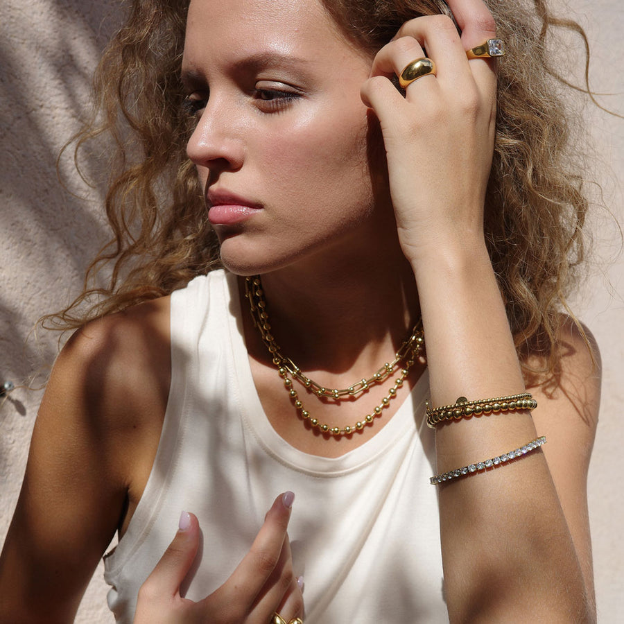 Gold link necklace and gold ball necklace shown layered on a model