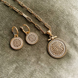 Gold necklace and earrings with circular pendants on a textured surface