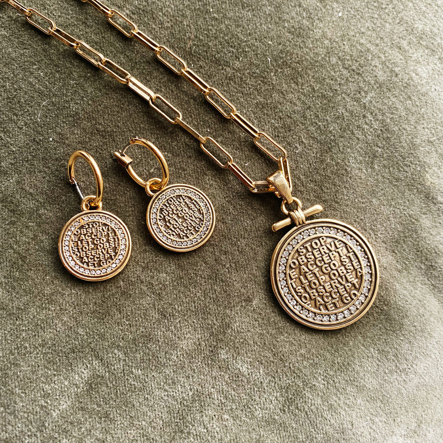 Gold necklace and earrings with circular pendants on a textured surface