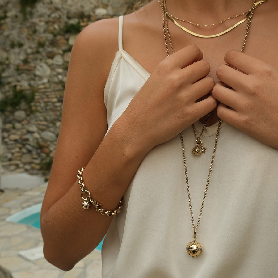 Person wearing gold jewelry including a necklace and bracelet, with a blurred natural background.
