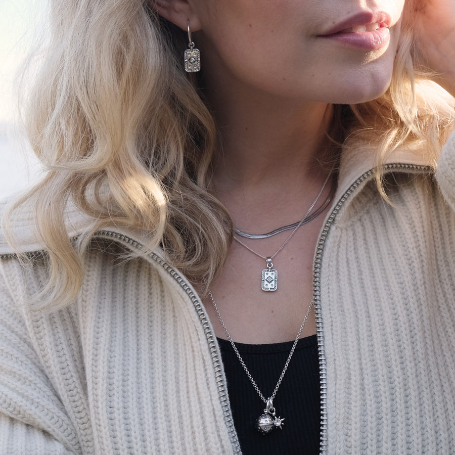 Close-up of a person wearing silver necklaces with pendants.