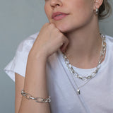 Woman wearing silver chain necklace and bracelet against a neutral background