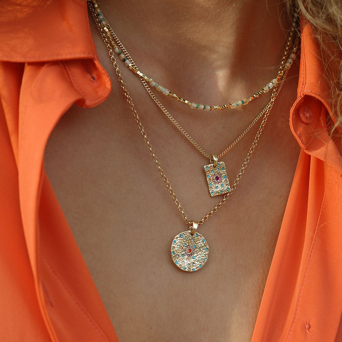Necklace with gold colorful pendants on a person wearing an orange shirt
