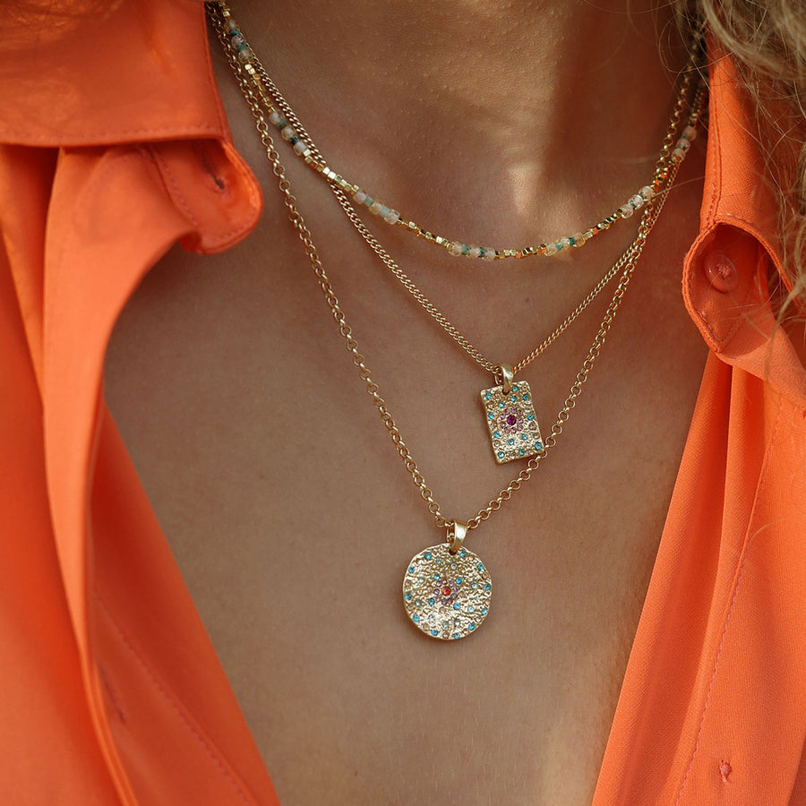 Necklace with gold colorful pendants on a person wearing an orange shirt