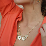 Close-up of a person wearing a gold necklace with circular pendants against an orange garment.