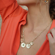 Close-up of a person wearing a gold necklace with circular pendants against an orange garment.