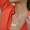 Close-up of a person wearing a gold necklace with circular pendants against an orange garment.