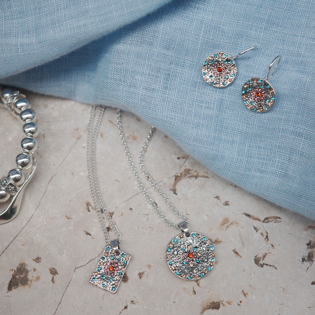 Jewelry set including necklace, earrings, and bracelet on a textured surface with blue fabric background.