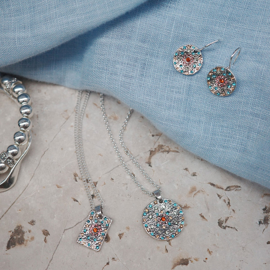 Jewelry set including necklace, earrings, and bracelet on a textured surface with blue fabric background.
