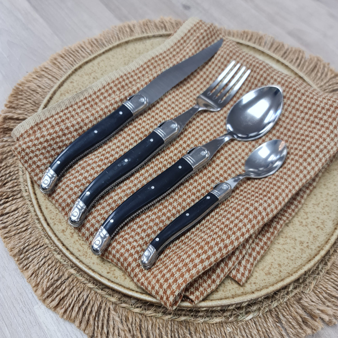 Set of silver cutlery with black handles on a woven mat
