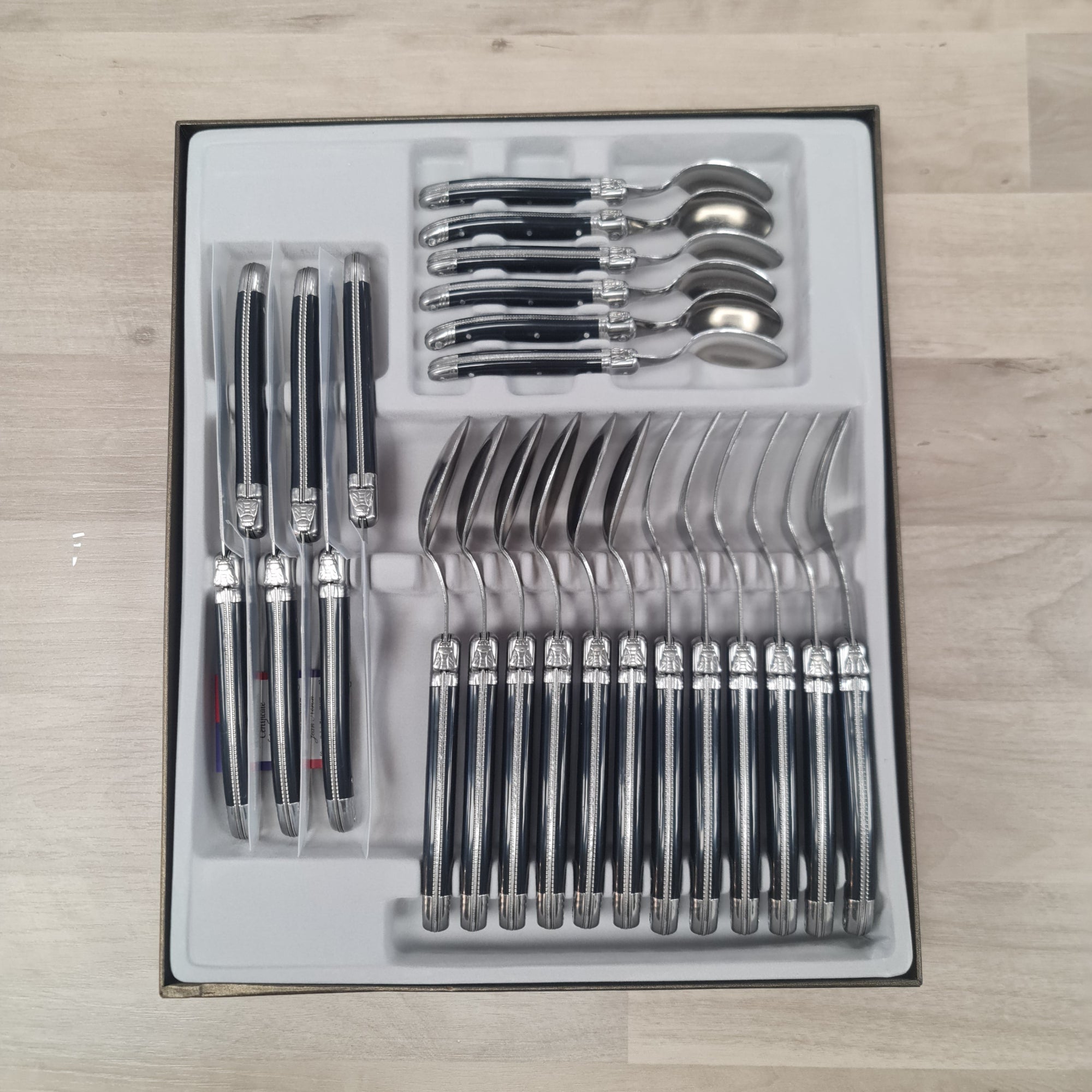 Set of laguiole cutlery including knives, forks,spoons and coffee spoons with black handles and bee icon