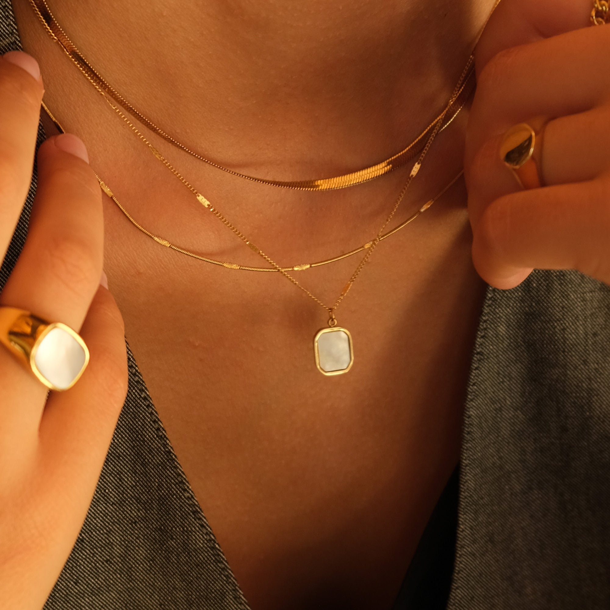 Close-up of a person wearing gold necklaces with a ring on a neutral background