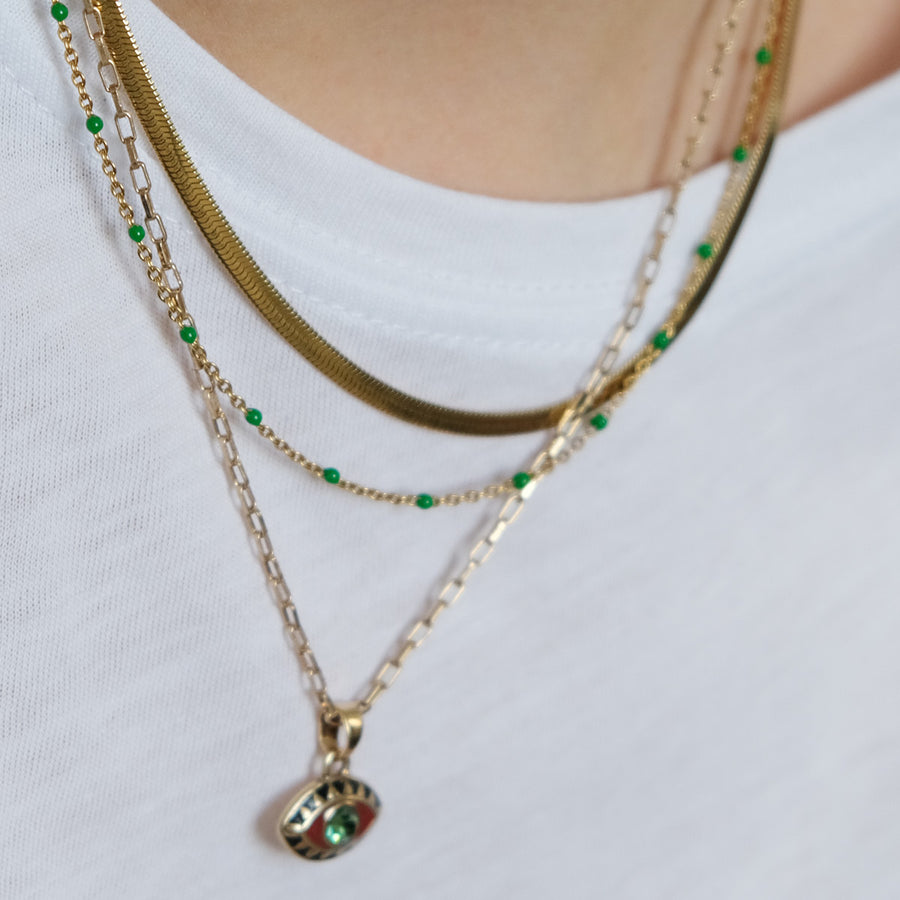 Close-up of a person wearing two gold necklaces with green beads on a white background