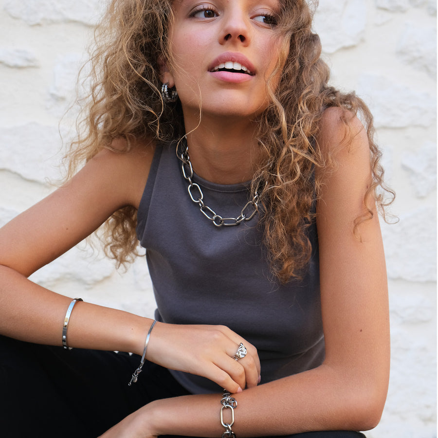 Woman wearing a silver chain necklace, bracelet, and ring against a white textured background