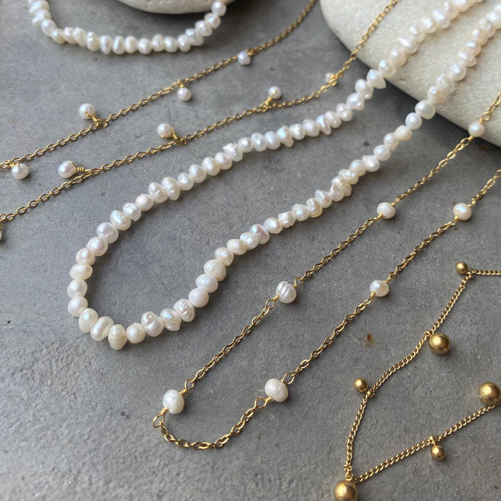 Pearl and gold chain necklaces on a textured surface