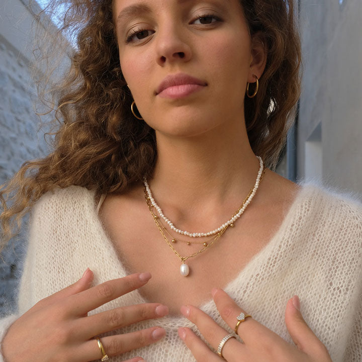 Woman wearing a pearl necklace and gold jewelry against a neutral background