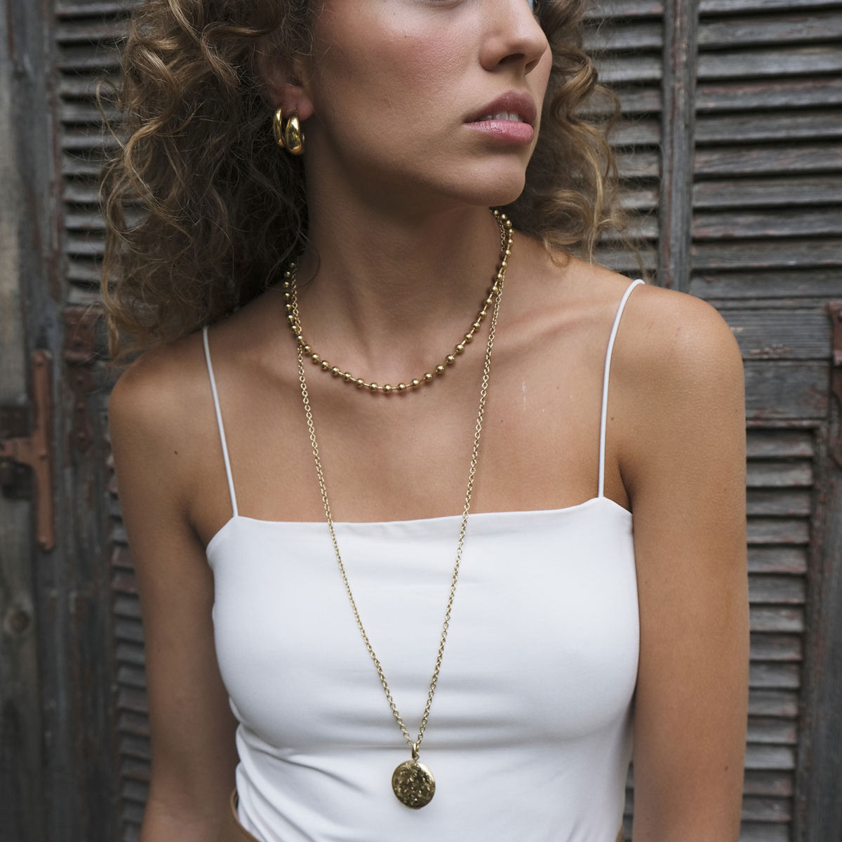 Woman wearing a Gold engraved round locket pendant on long chain