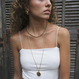 Woman wearing a Gold engraved round locket pendant on long chain