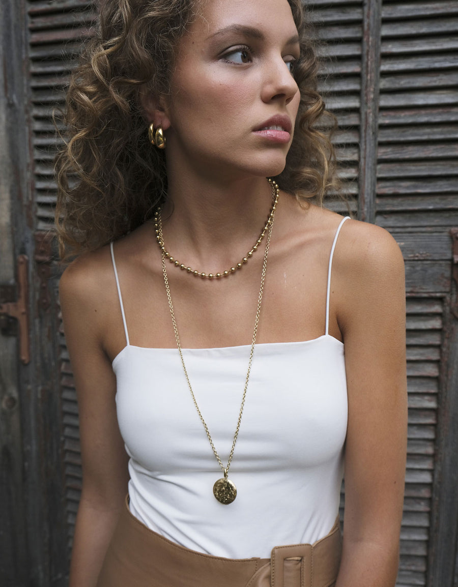 Woman wearing a Gold engraved round locket pendant on long chain