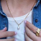 Gold chain necklace with a pearl pendant worn by a person.