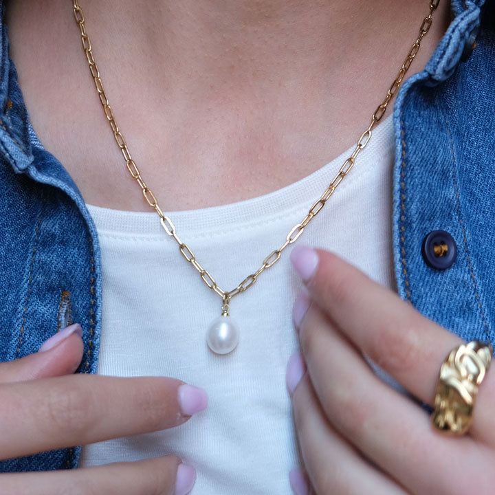 Gold chain necklace with a pearl pendant worn by a person.