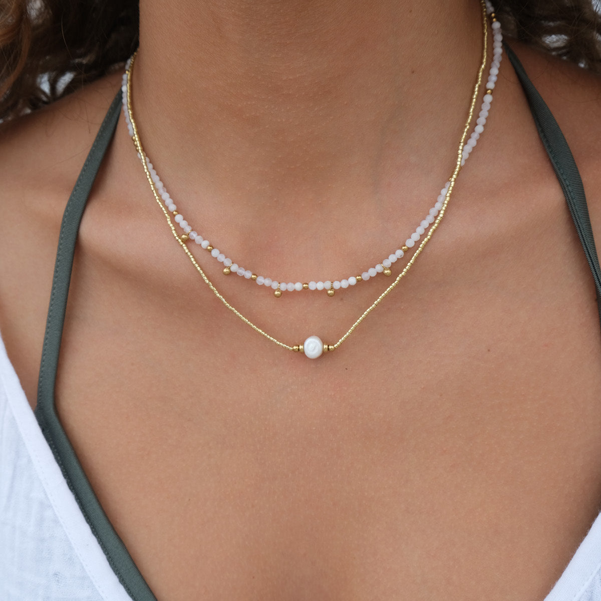 Close-up of a person wearing a delicate gold necklace with a pearl pendant.