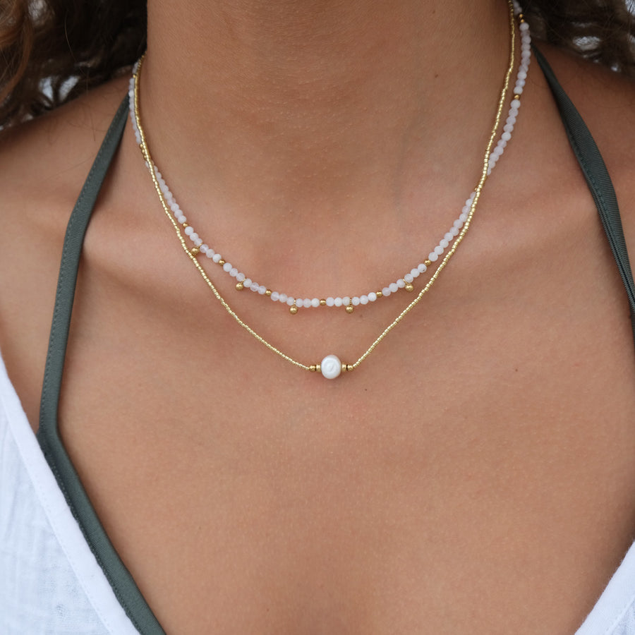 Close-up of a person wearing a delicate gold necklace with a pearl pendant.