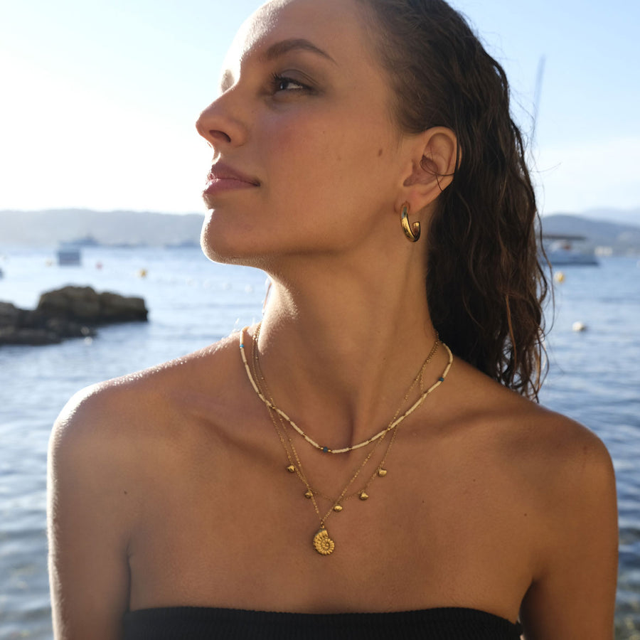 Woman wearing gold jewelry with a body of water in the background