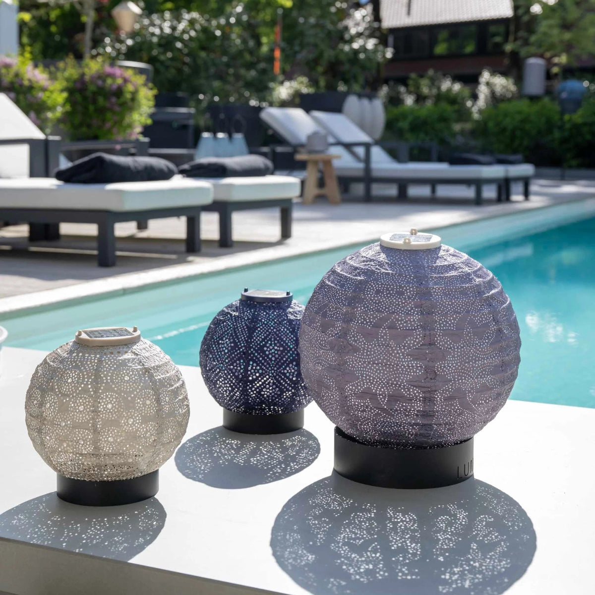 Group of three round lamps in purple and taupe sheds beside a pool on lumiz lamp stands