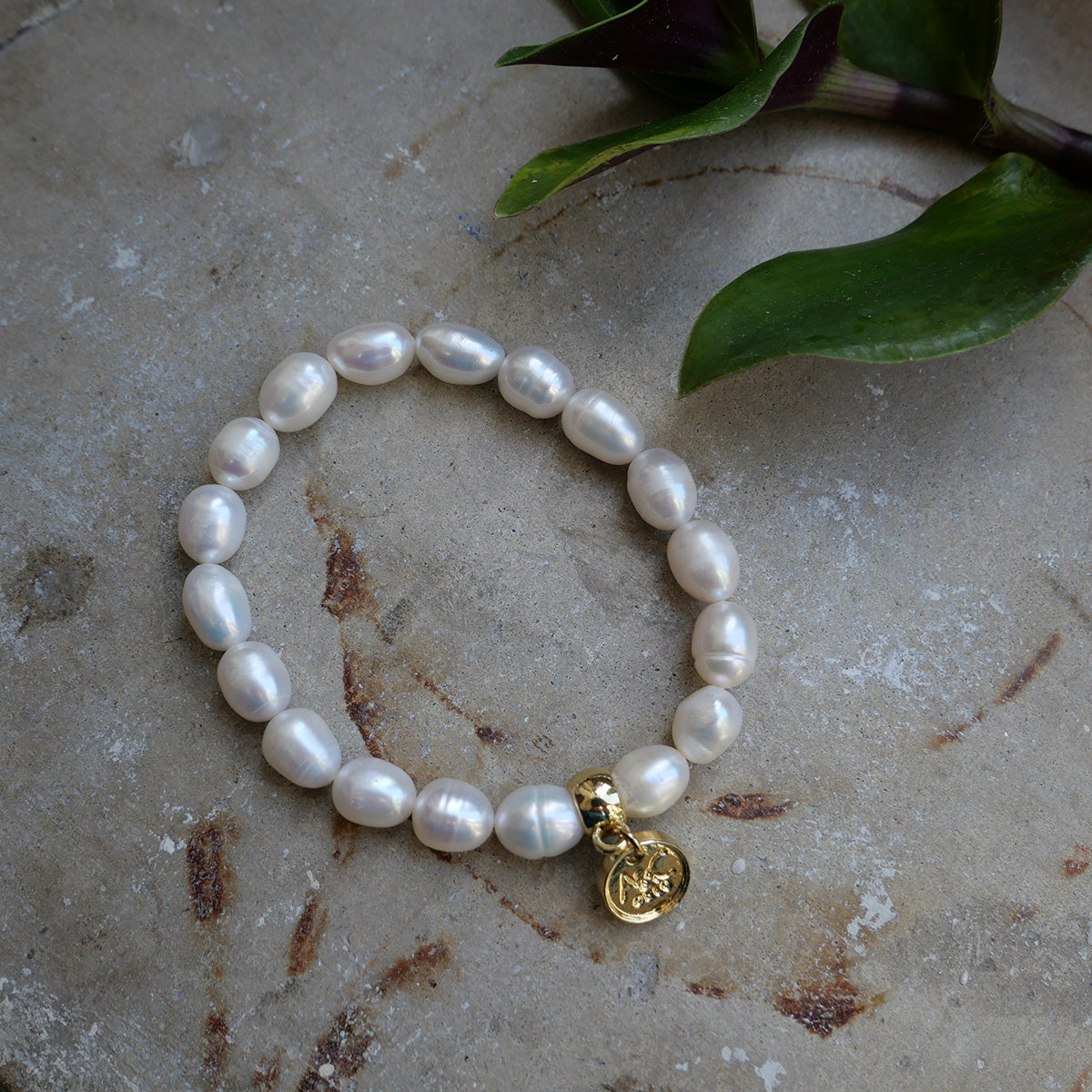 Pearl bracelet with a gold charm on a textured surface with leaves.