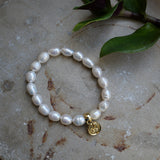 Pearl bracelet with a gold charm on a textured surface with leaves.