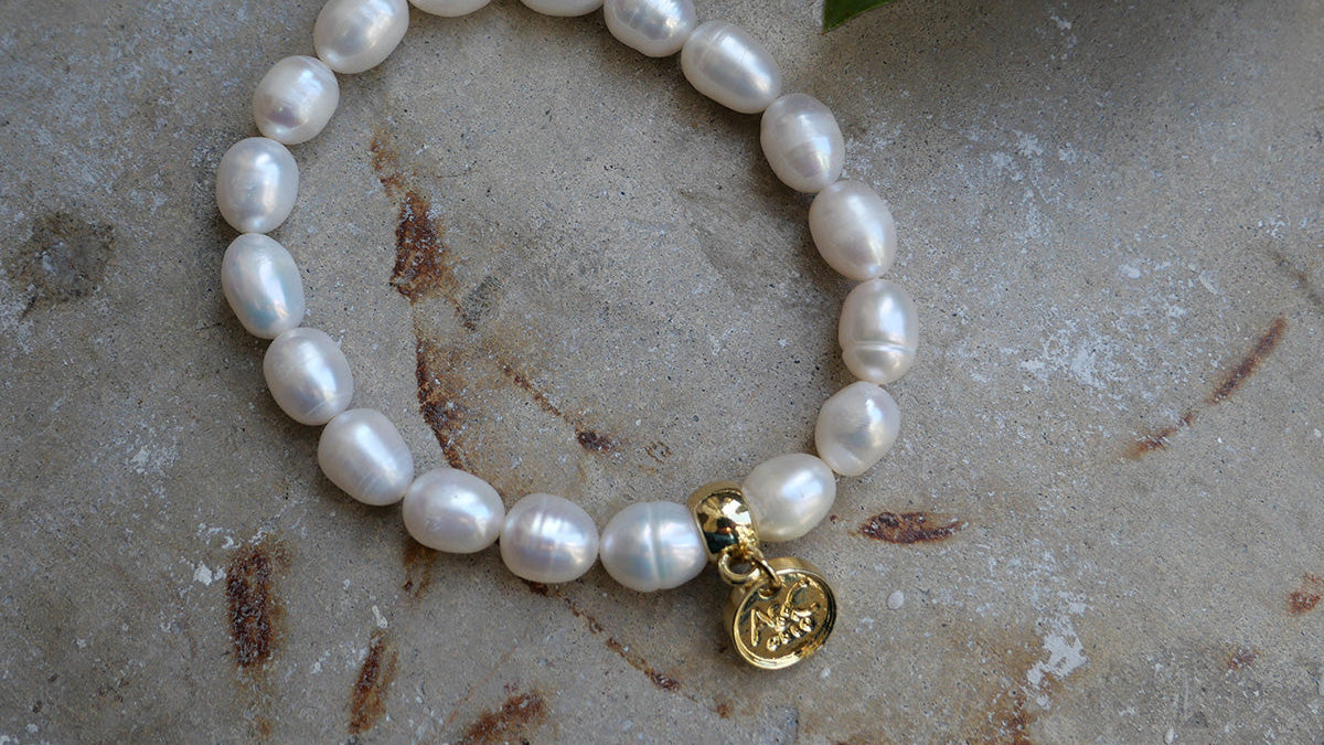 Pearl bracelet with a gold charm on a textured surface with leaves.