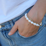 Hand wearing a pearl bracelet with a gold clasp on a denim background