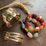 Multicolored beaded bracelet and gold cuff bracelet on a textured surface