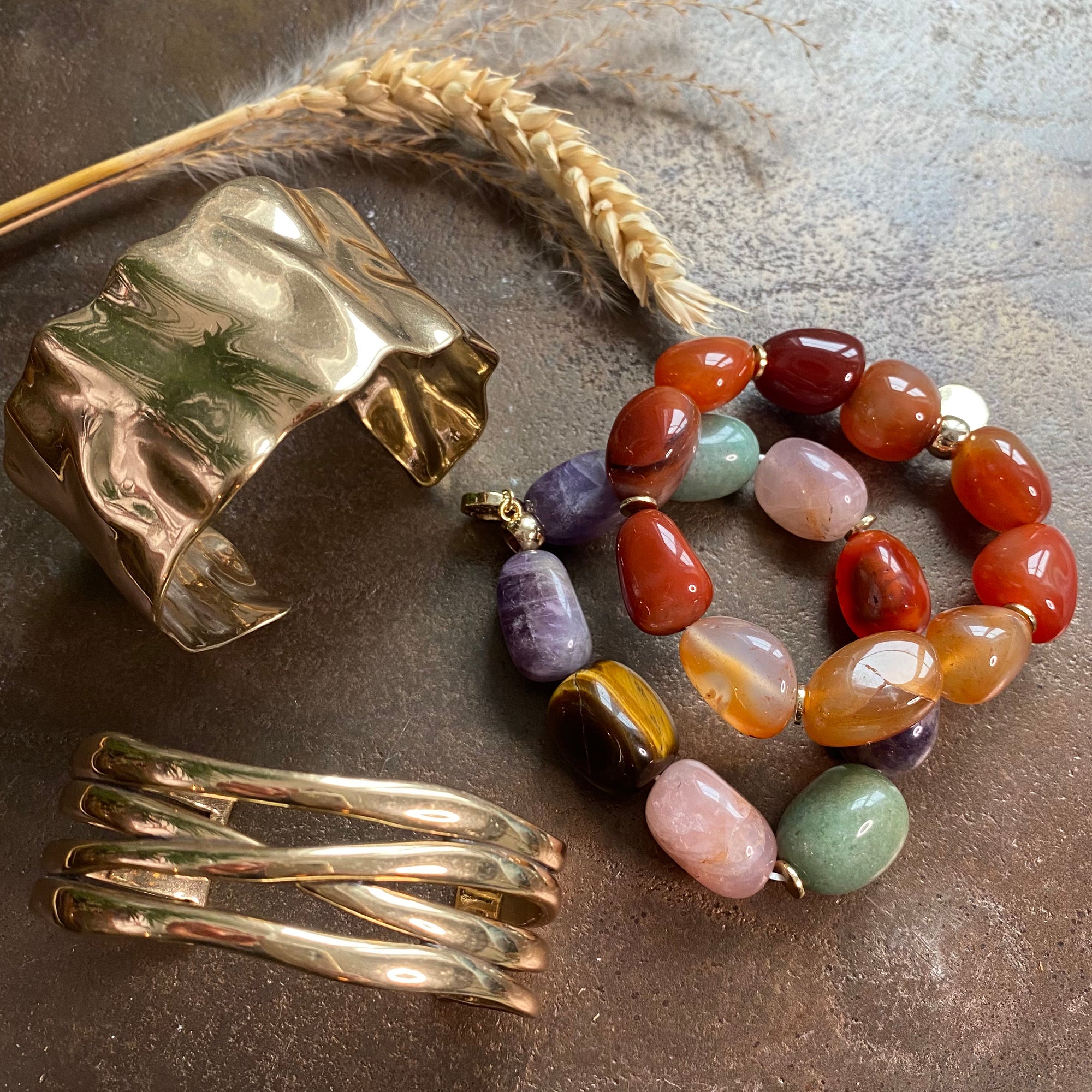 Multicolored beaded bracelet and gold cuff bracelet on a textured surface
