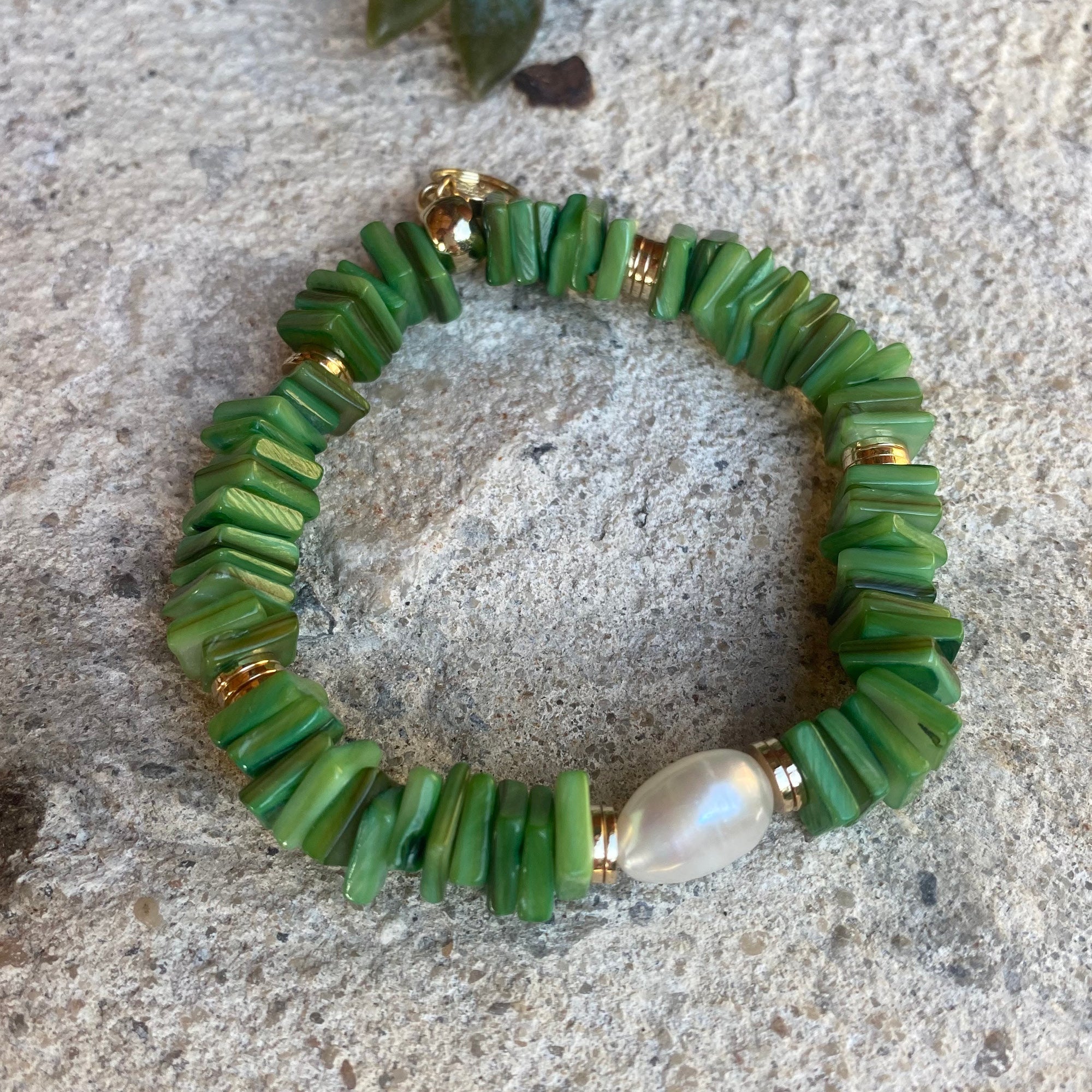 Green shell bracelet with a pearl accent on a stone surface